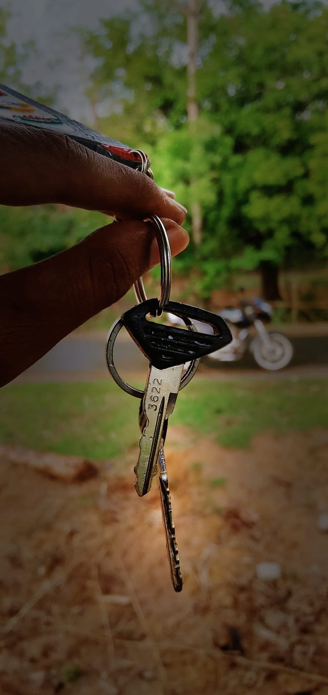 Hand holding motorcycle keys with a blurred bike in the background, showing sharp metallic textures and bokeh.