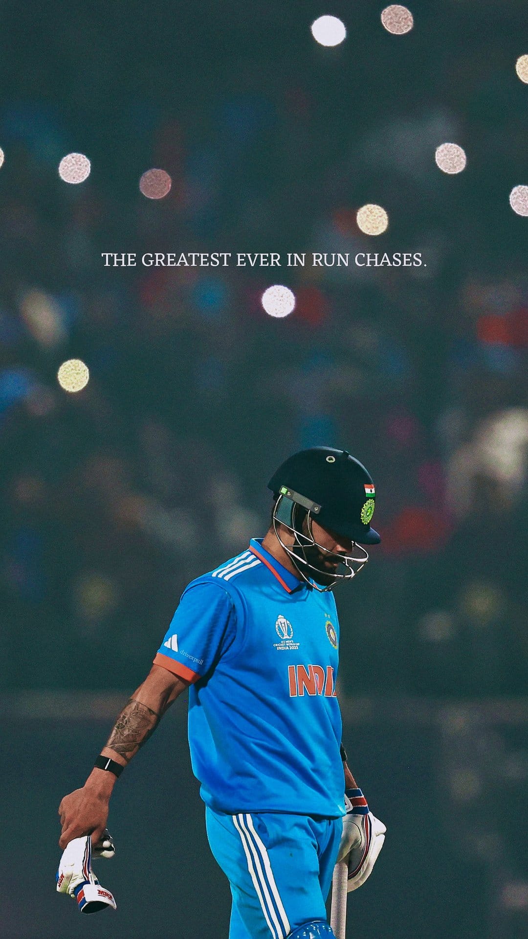 Virat Kohli in a blue Indian cricket jersey stands before blurred stadium lights with an intense expression.