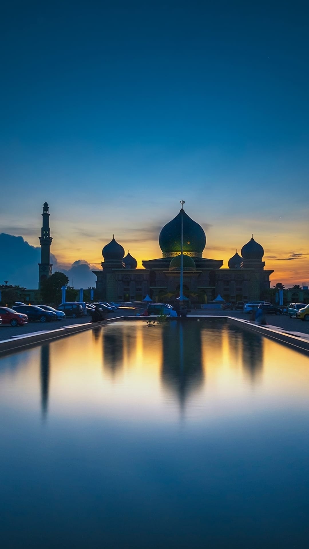 An-Nur Great Mosque silhouette reflects in still water under a blue and orange sunrise sky during the early dawn.