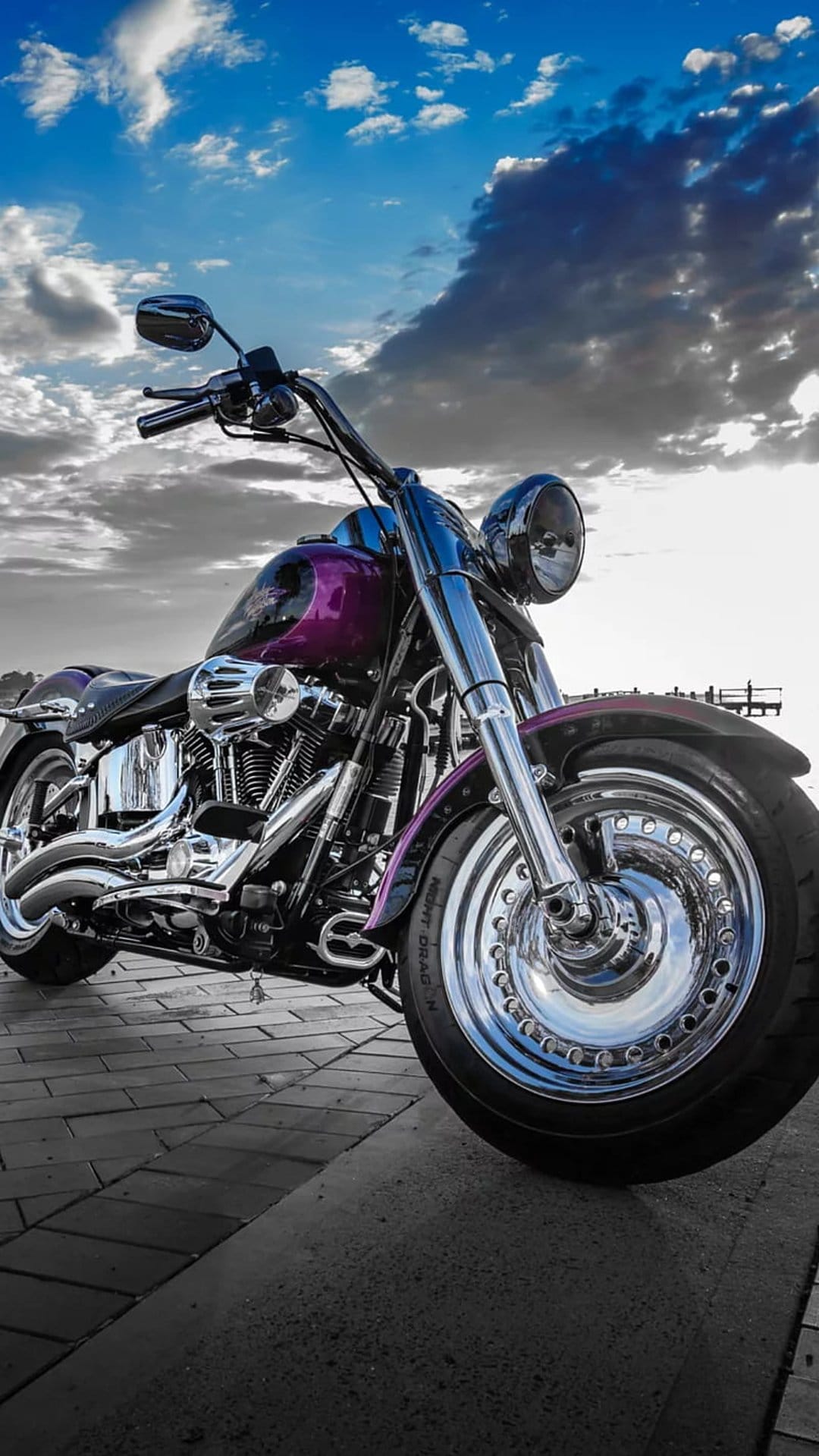 Purple Harley Davidson motorcycle with chrome engine parts on a brick path under dark, swirling storm clouds.