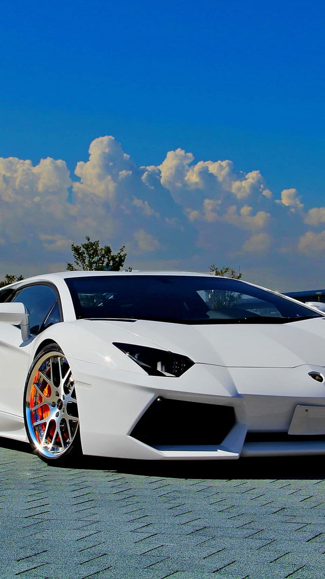 White Lamborghini Aventador featuring chrome wheels and orange accents under a blue sky with fluffy clouds.