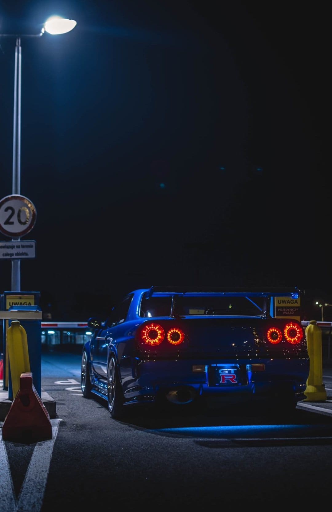 Blue Nissan Skyline GT-R R34 at night with glowing red circular taillights and neon blue underglow.