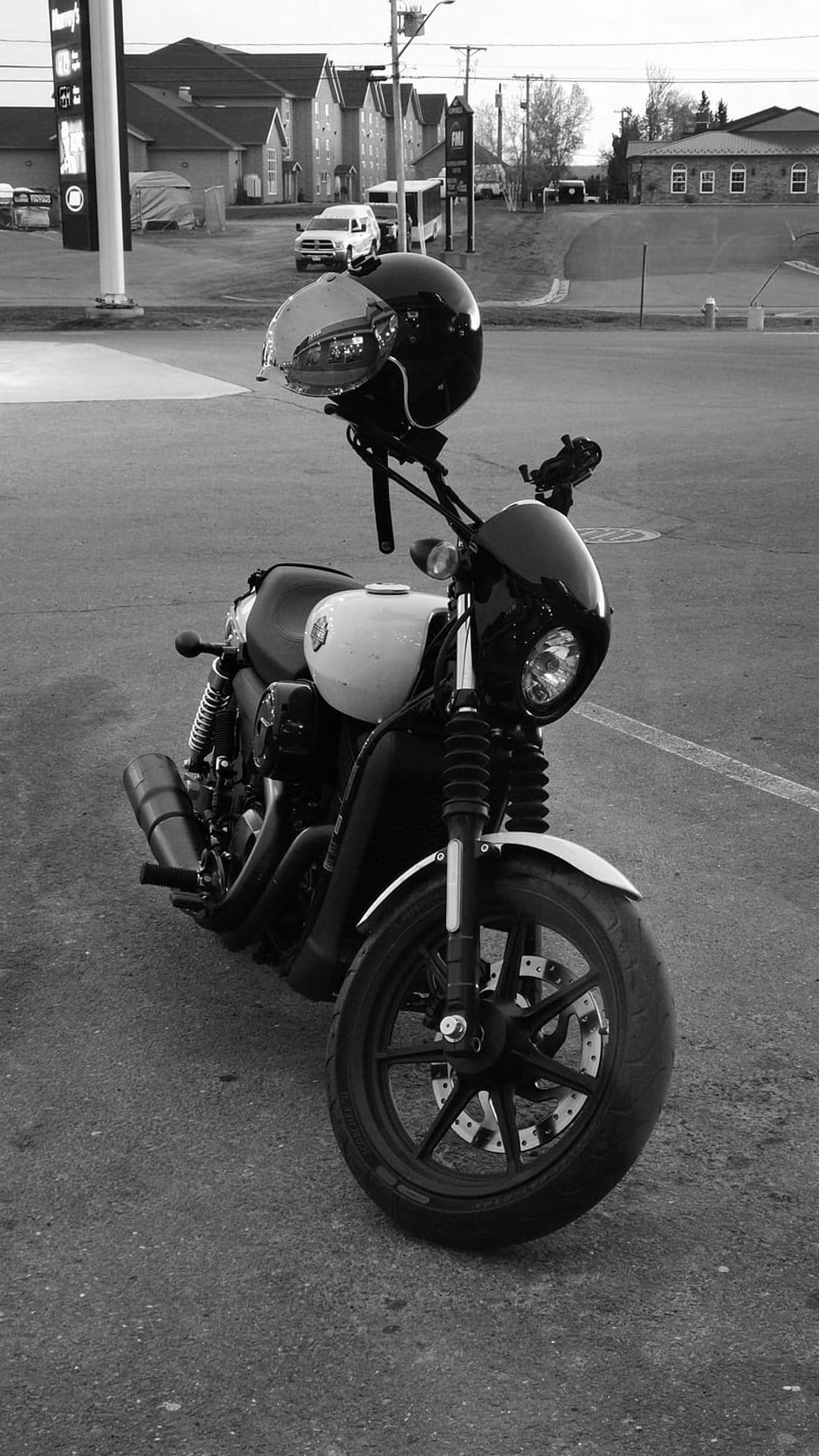 Modern motorcycle with a helmet on the handlebars sits on an urban street in high-contrast black and white.