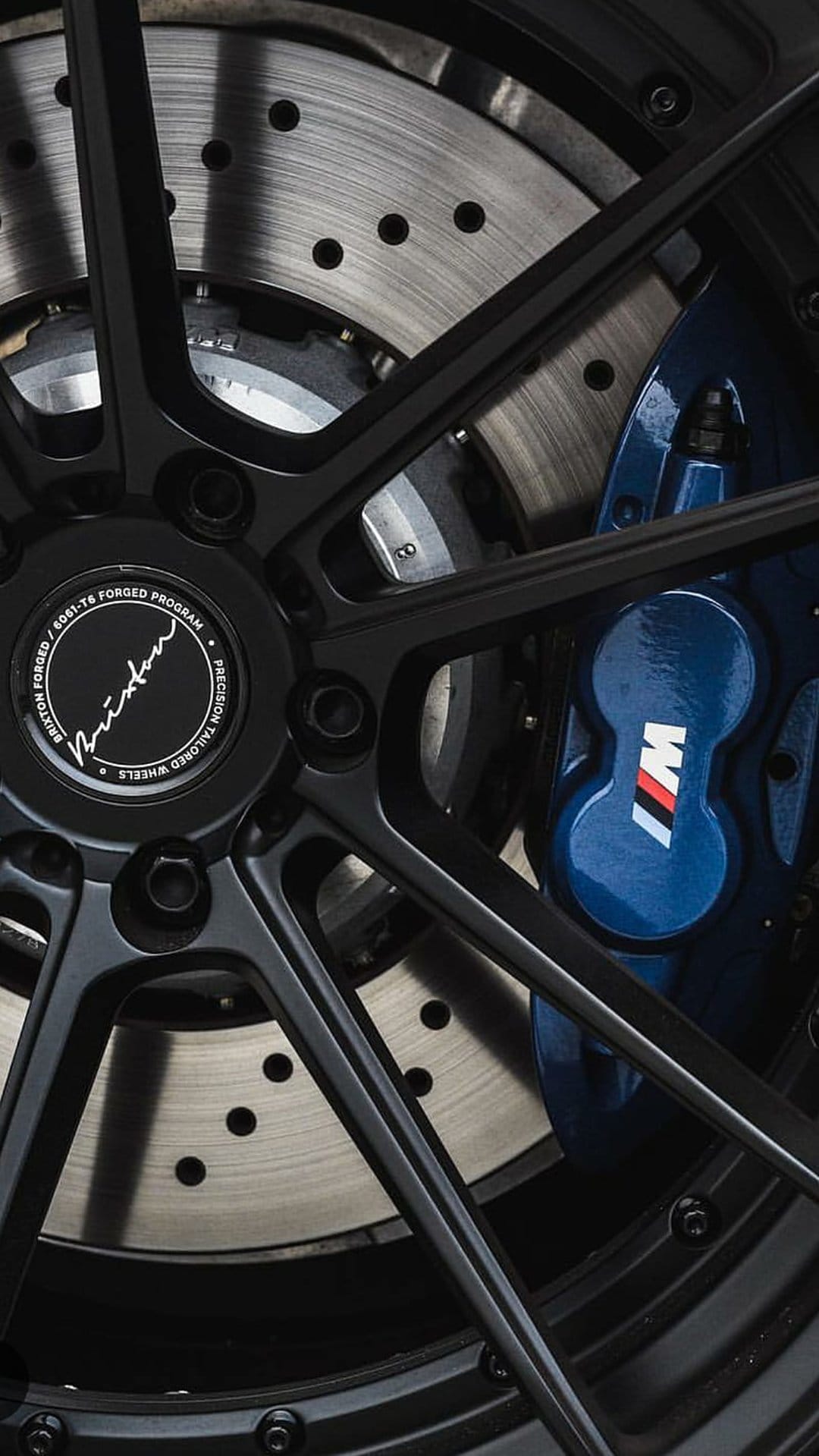 Blue BMW M Performance brake caliper with tricolor logo sits behind a black multi-spoke alloy wheel and rotor.