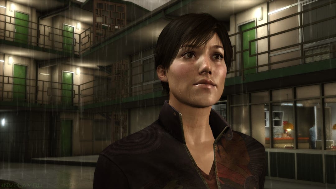 Woman with wet short hair looking up in front of a green-doored motel courtyard at night in the rain.