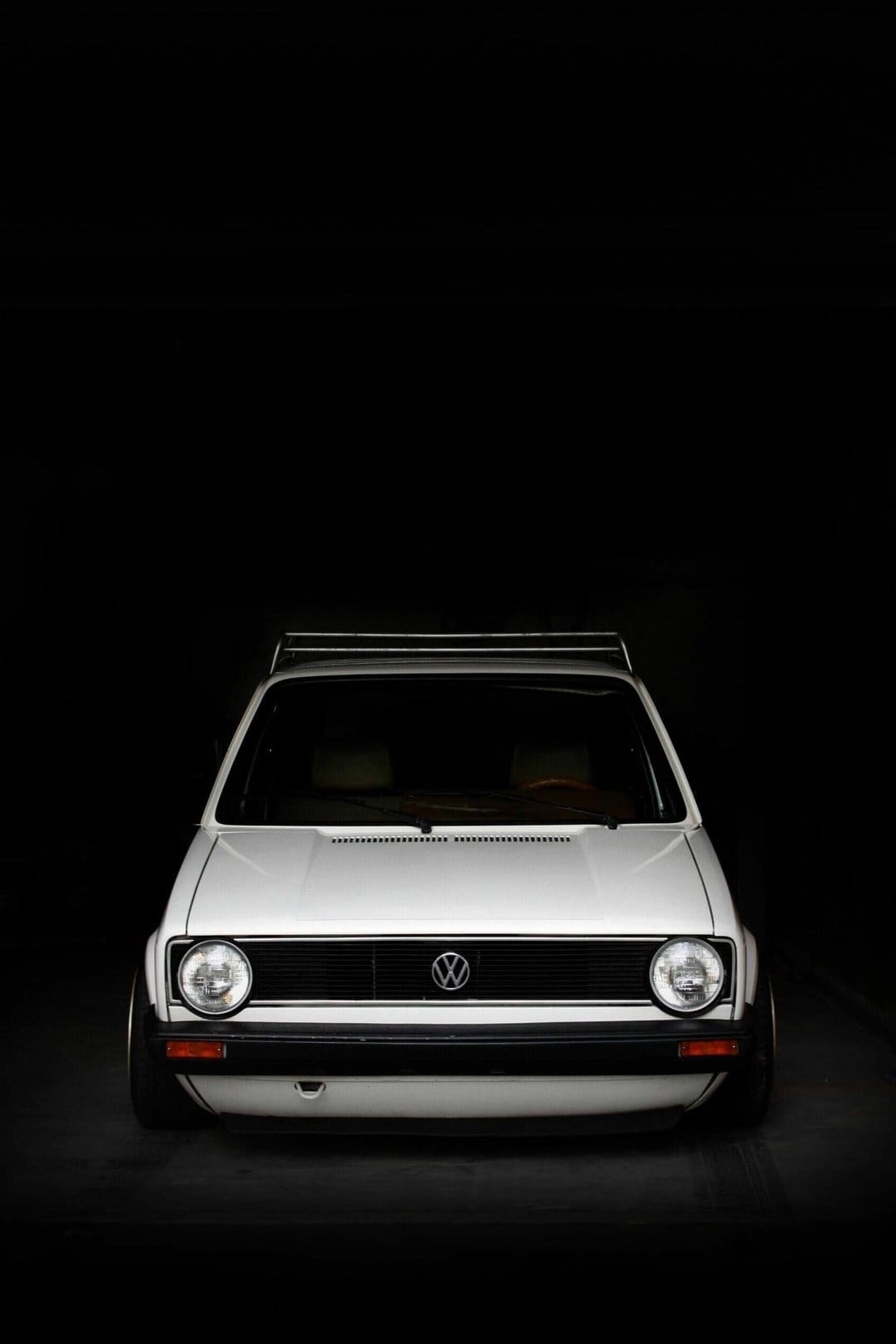 White classic Volkswagen car with round headlights and roof rack centered against a dark black background.