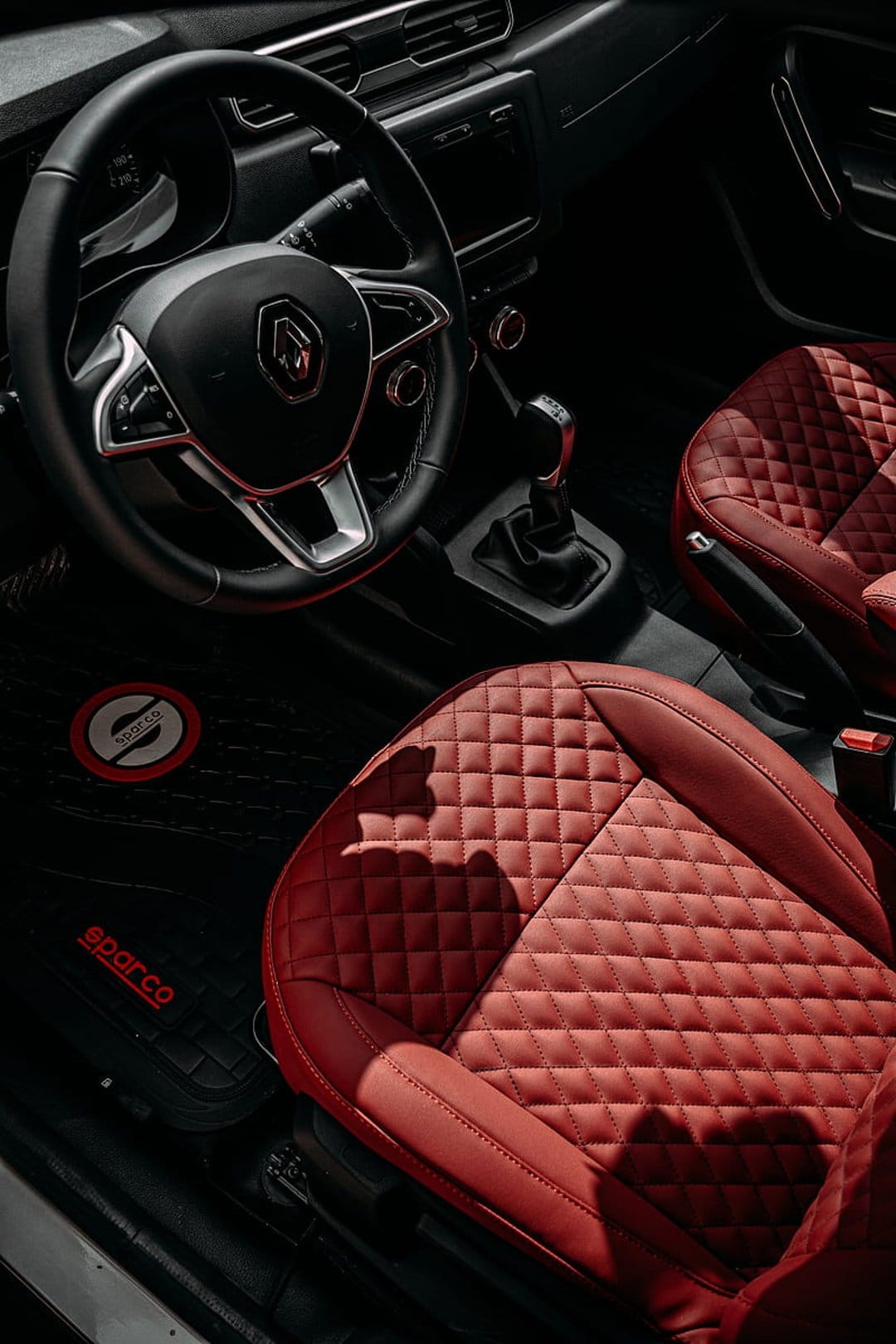 Red quilted leather car seats and a black steering wheel with a silver logo fill a luxury vehicle interior.