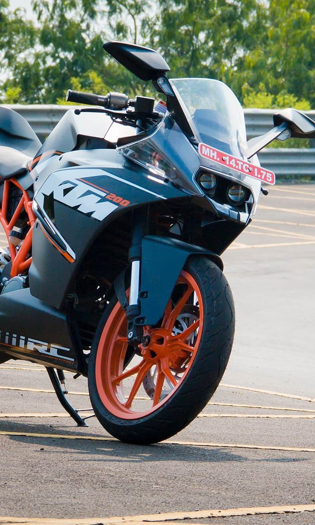 KTM RC 200 motorcycle showcasing orange alloy wheels, black fairing, and suspension against a green forest.