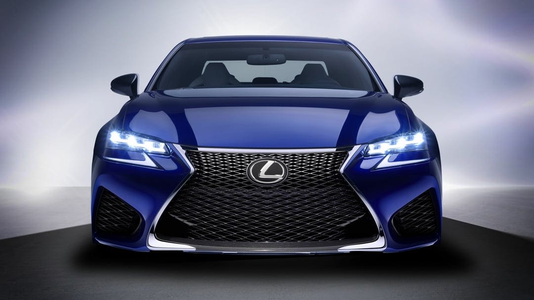 Front view of a blue Lexus sedan with glowing LED headlights and a large black mesh spindle grille.