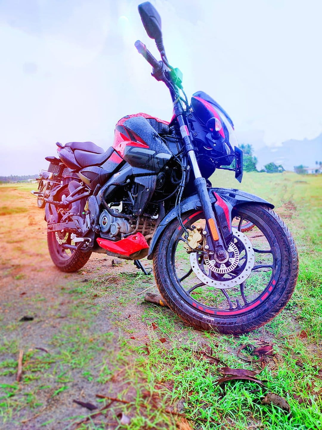 Crimson and black sports motorcycle parked on a dirt path with tall grass under a hazy sky during daytime.