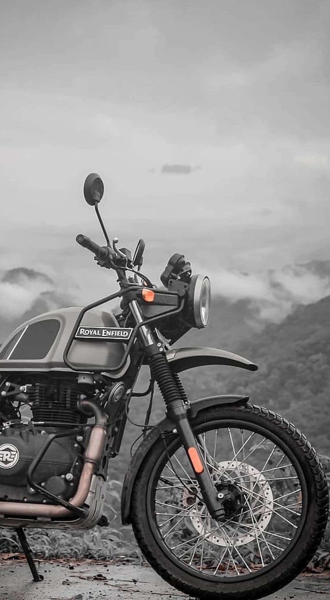 Royal Enfield Himalayan motorcycle parked on rocky terrain with foggy mountains under a cloudy monochrome sky.