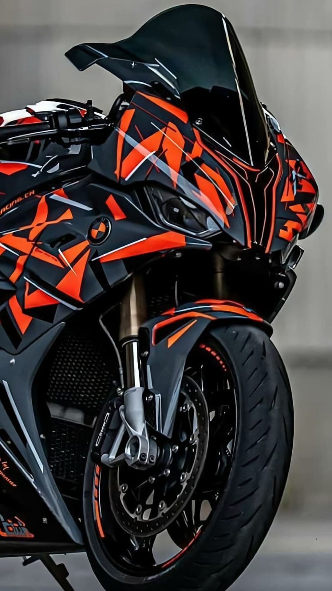 BMW S1000RR motorcycle with orange geometric patterns, matte black fairing, and a tinted windshield close-up.