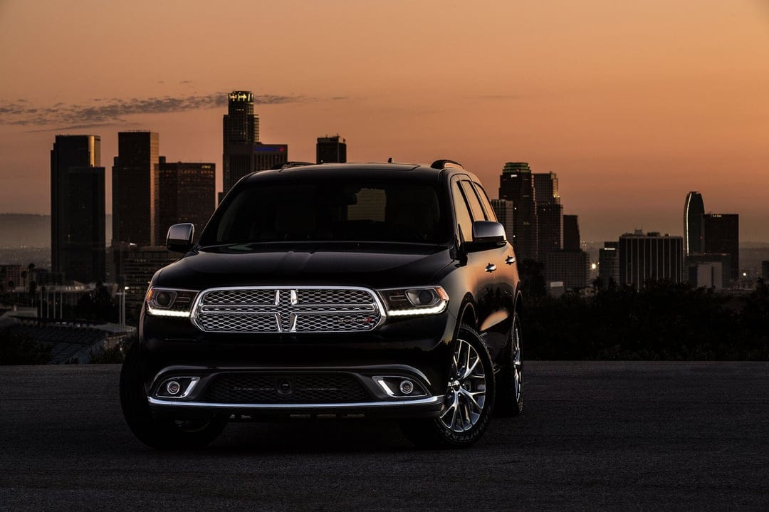 Black Dodge Durango SUV parked on a hill with the Los Angeles skyline under an orange sunset sky.