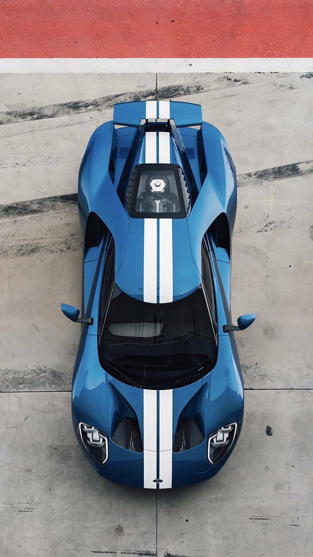 Blue Ford GT race car with dual white stripes parked on concrete beside a red line from a top-down view.