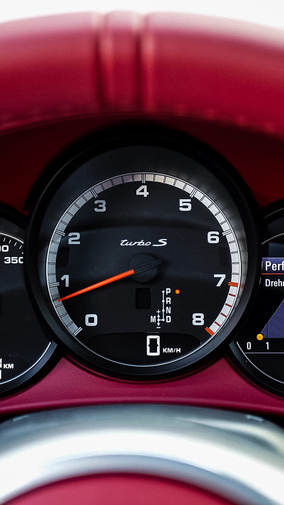 Porsche Turbo S tachometer with an orange needle and digital performance display set against a red dashboard.