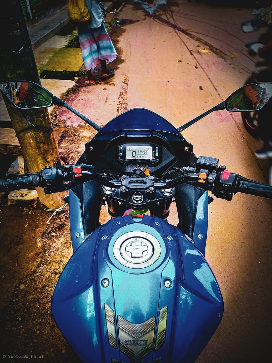 Blue Suzuki motorcycle handlebars and digital speedometer display seen from a rider's perspective on a sunny day.