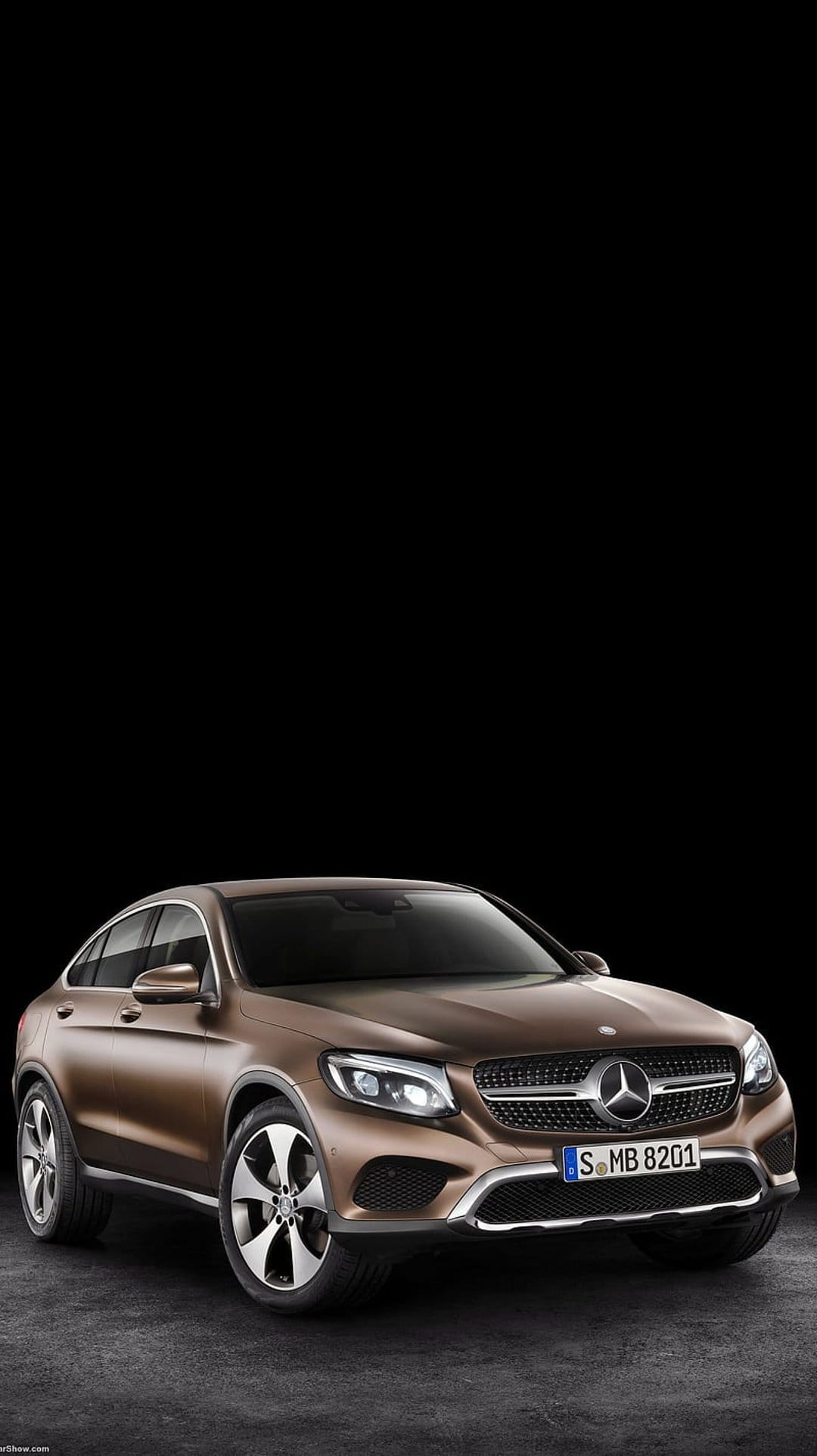 Brown Mercedes-Benz GLC Coupe SUV with illuminated headlights and a chrome grille against a black studio background.