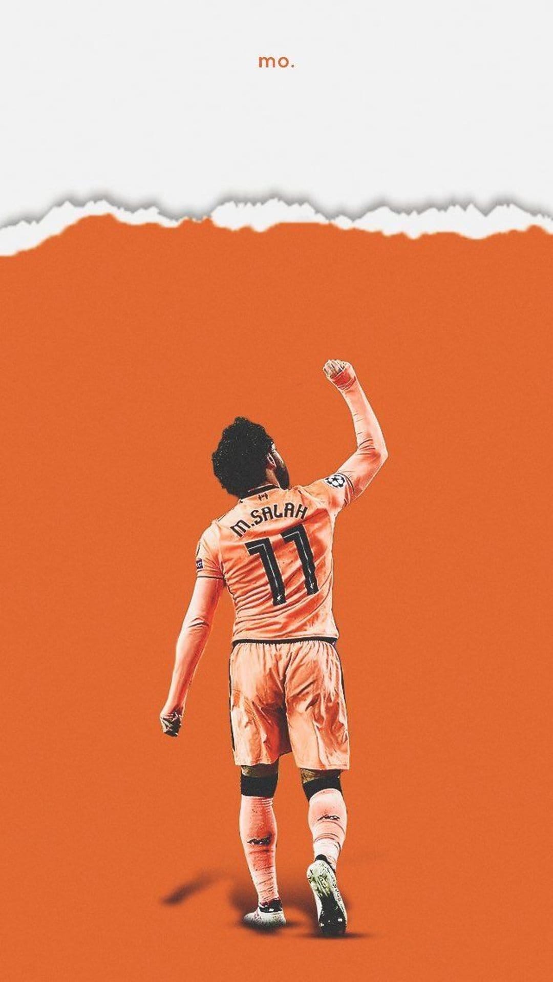 Mohamed Salah stands from behind with a raised fist wearing an orange number eleven kit on an orange backdrop.