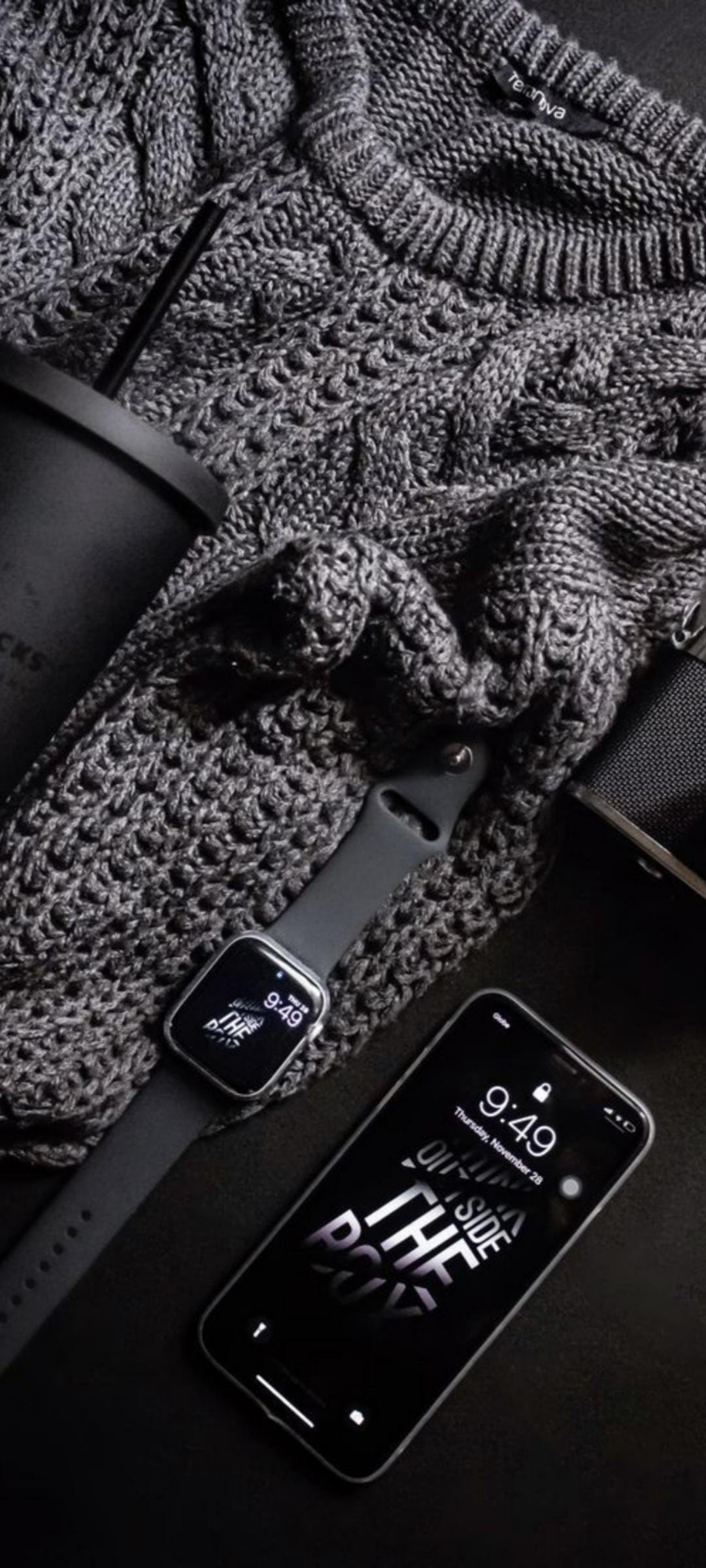 Dark gray cable knit sweater textured fabric next to a black smartwatch and smartphone on a dark surface.