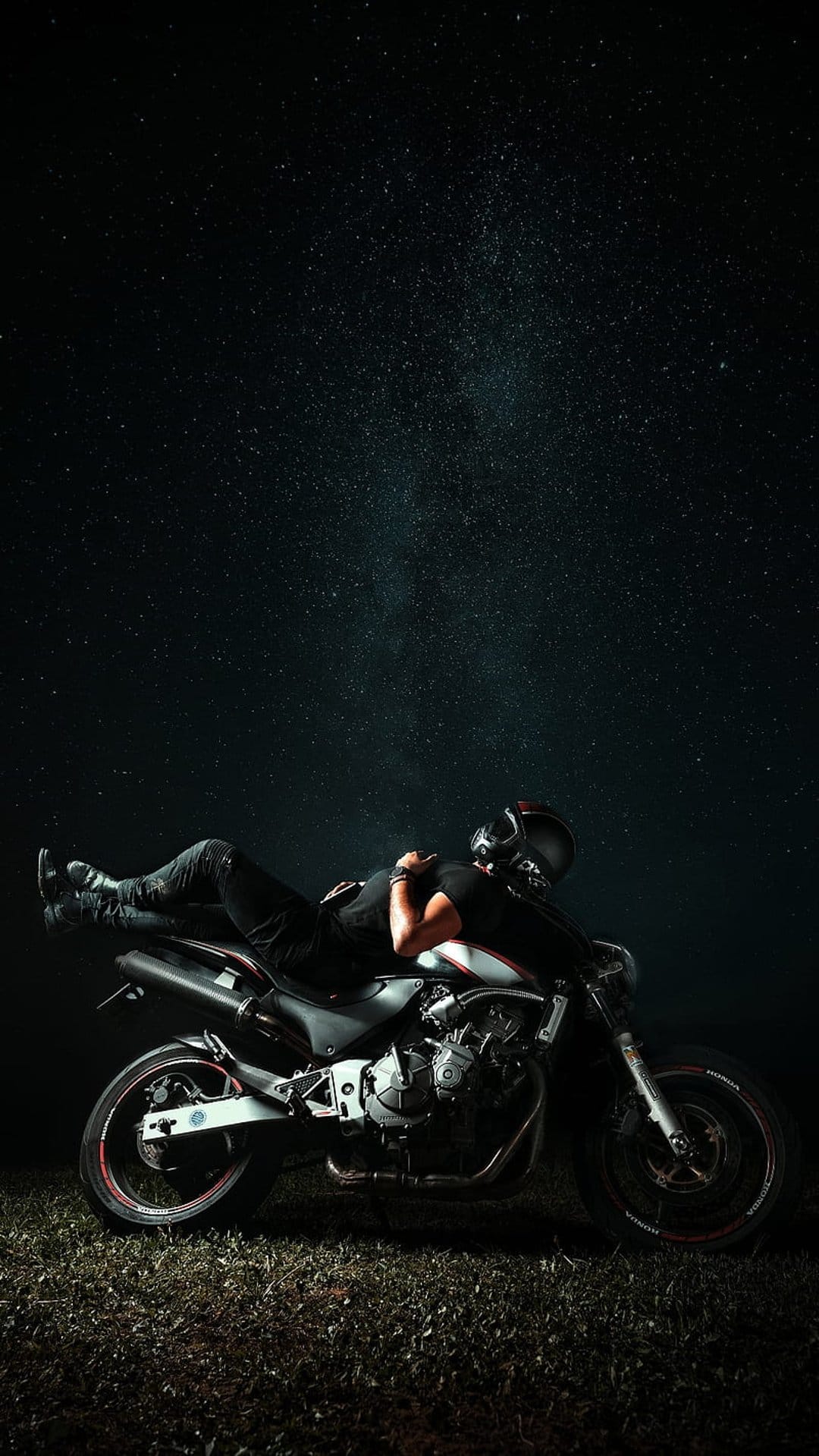 Biker in full riding gear reclines on a motorcycle seat beneath a dense field of shimmering night stars.