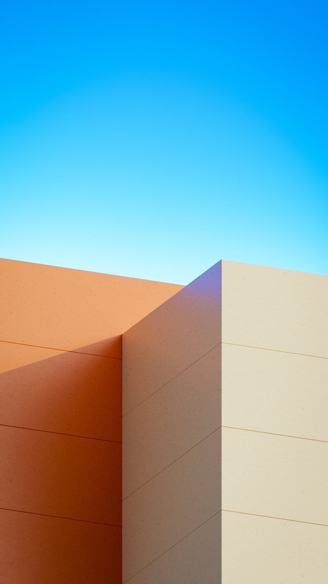 Orange and cream building corner intersects against a clear blue sky, showing clean architectural lines and shadows.