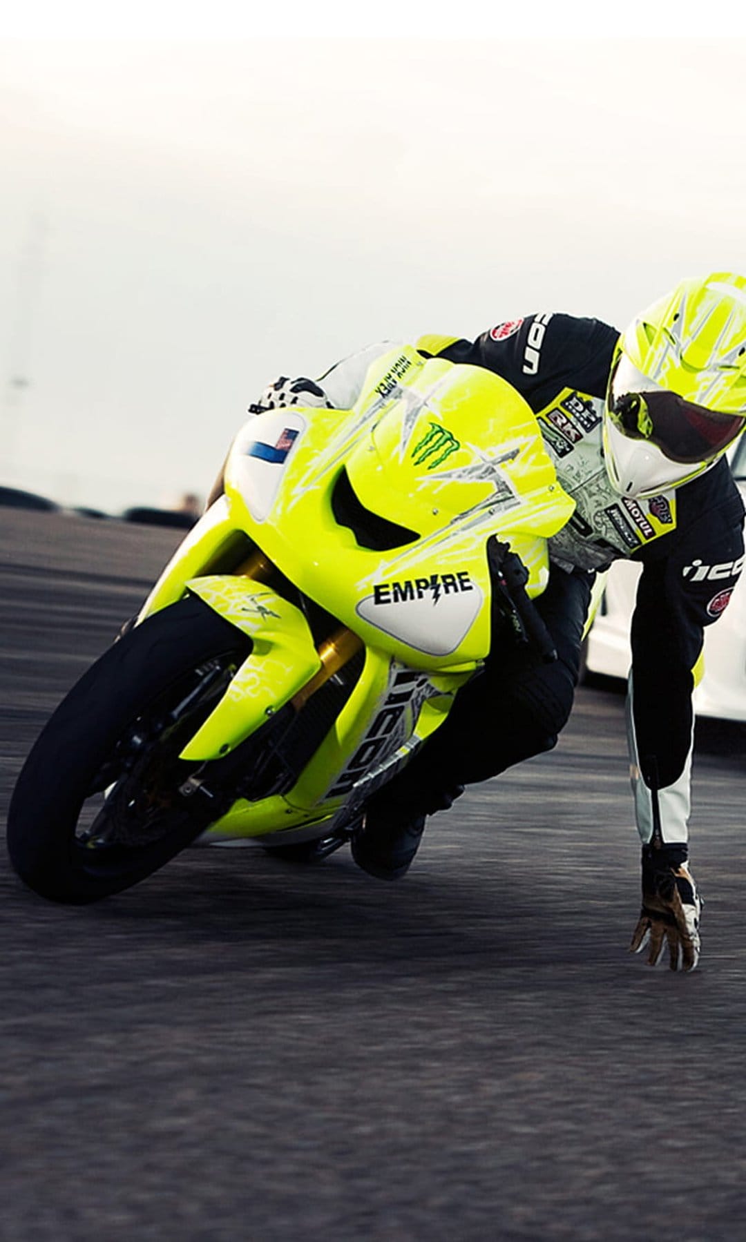 Motorcyclist in yellow racing gear leans a neon sportbike into a sharp asphalt turn with visible motion blur.