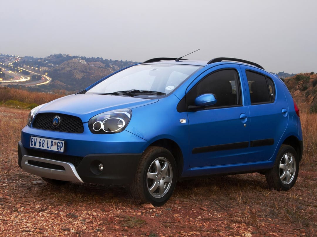Blue compact crossover car parked on a rocky hill overlooking a highway with lights at dusk under a grey sky.