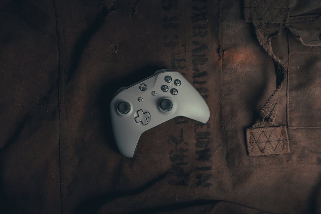 White Xbox controller on a dark, worn fabric surface with moody lighting highlighting the joysticks and buttons.