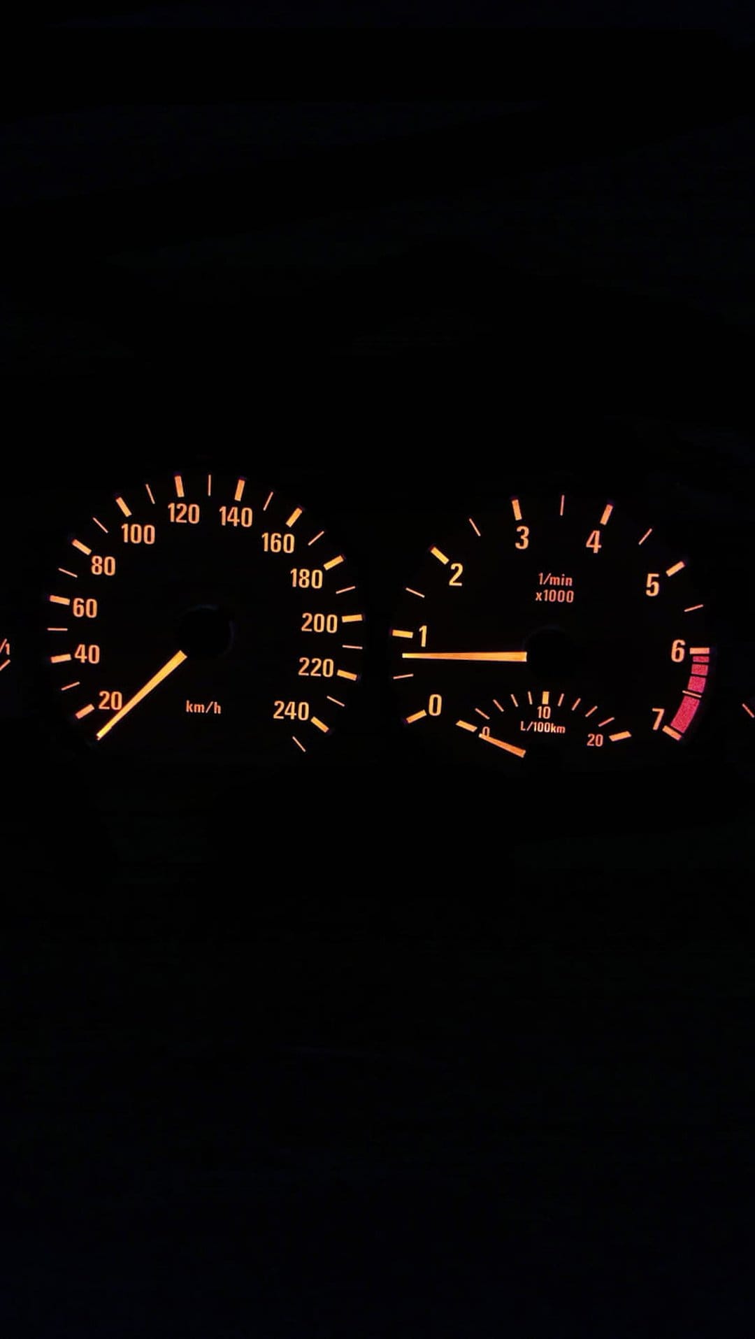 Glowing orange speedometer and tachometer dials shine against a dark vehicle interior during a night drive.