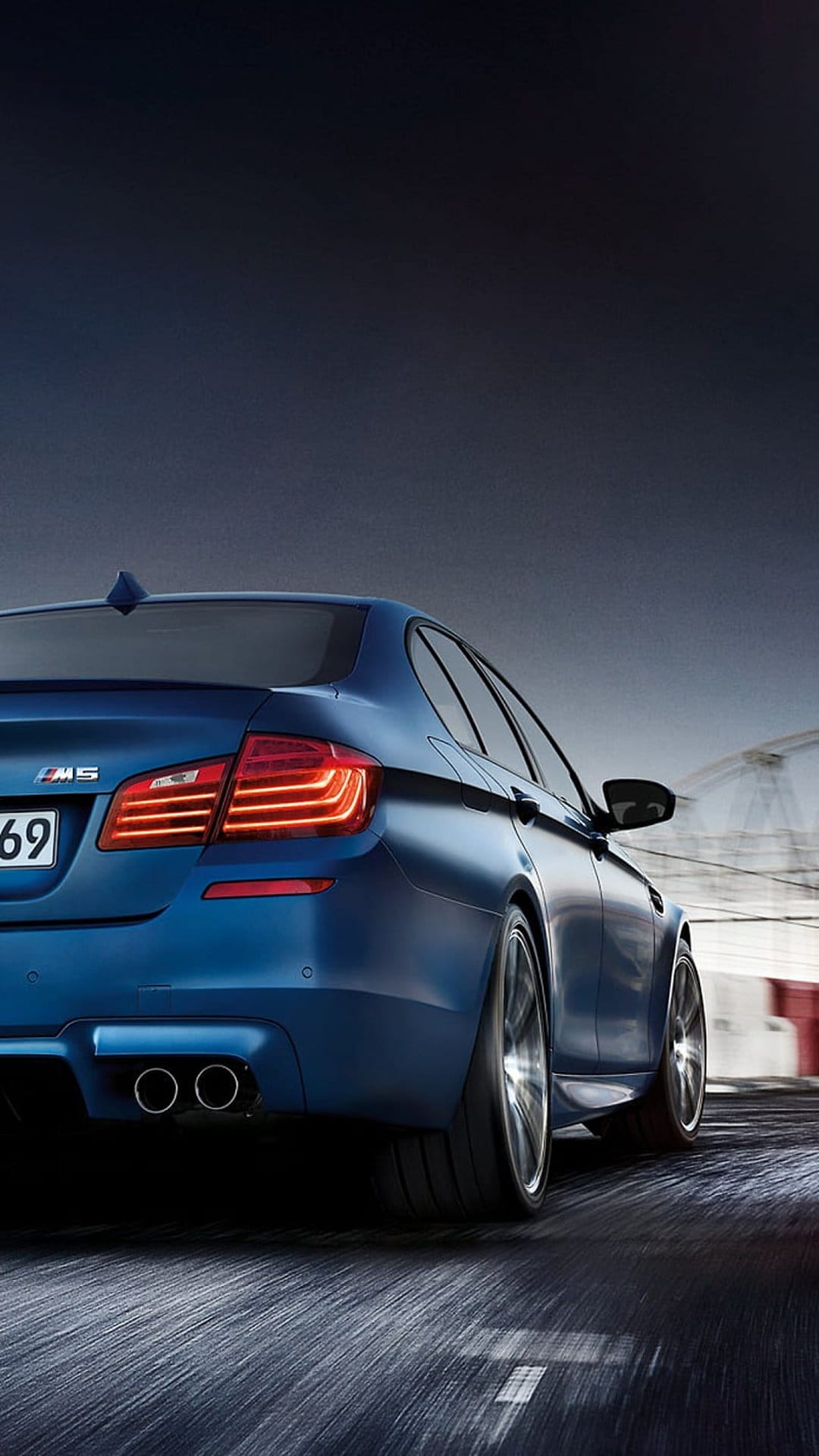 Blue BMW M5 sports sedan with glowing taillights accelerating on a racetrack with heavy motion blur effects.