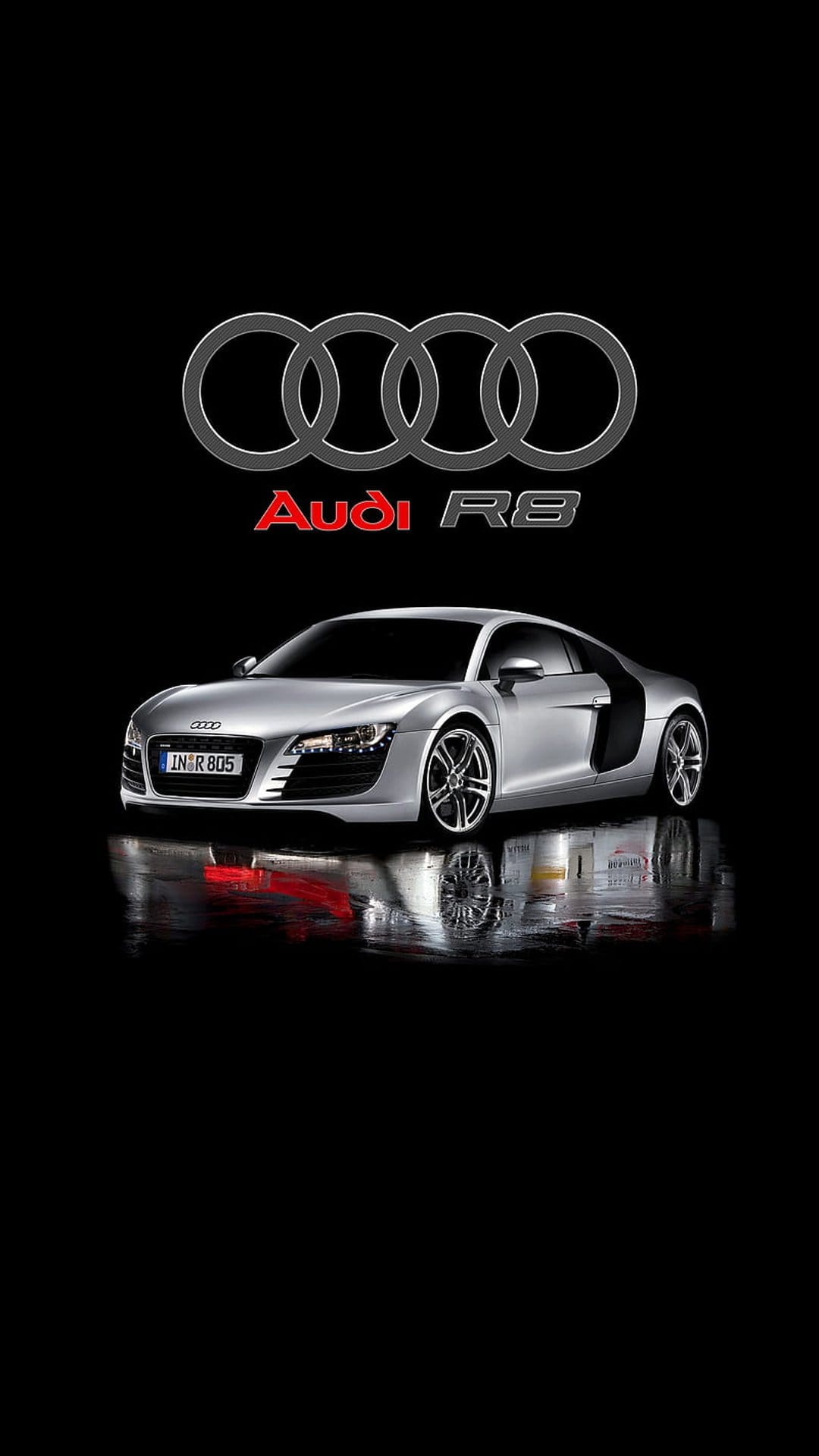 Audi R8 supercar in silver reflects on a glossy floor beneath the Audi rings logo on a black background.