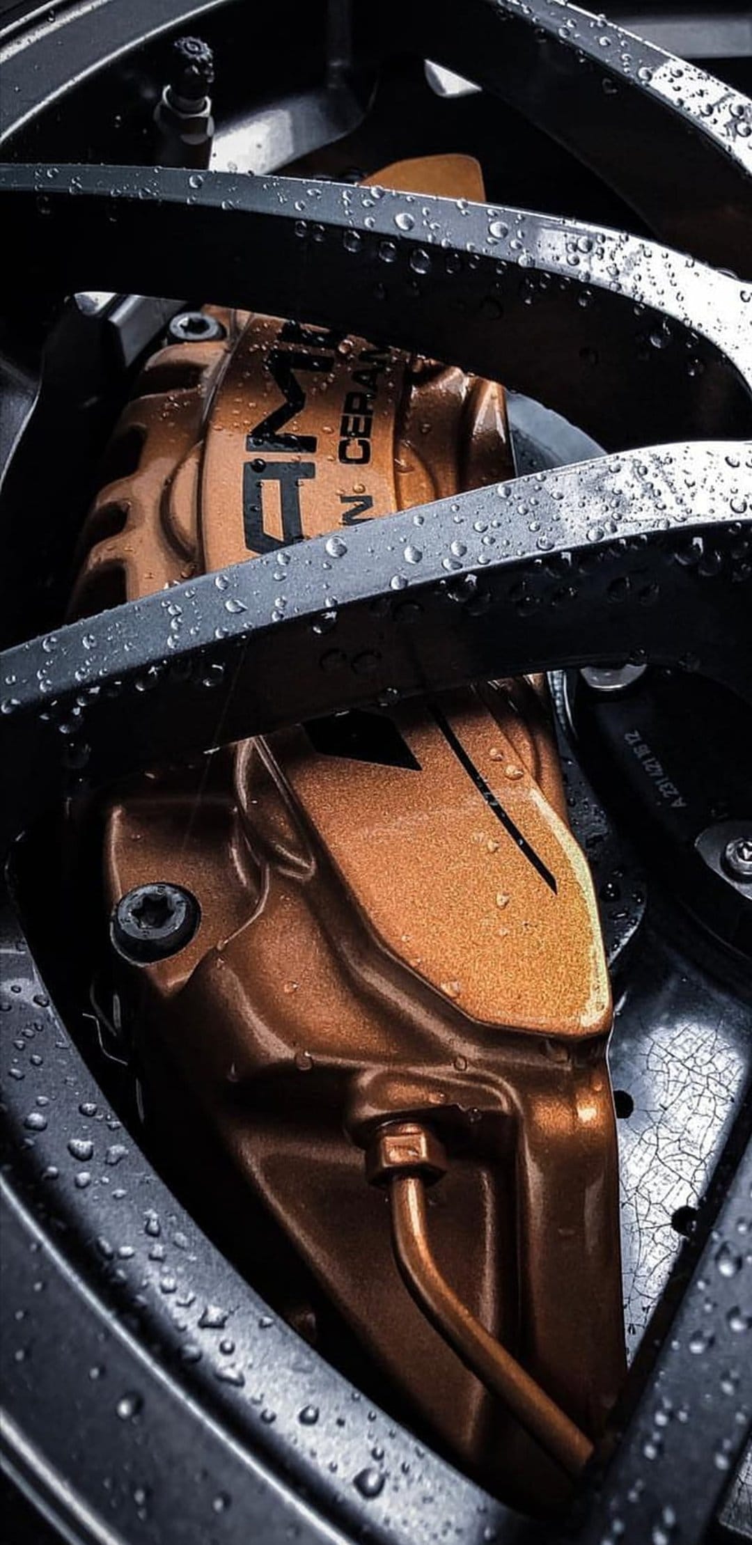 Gold AMG ceramic brake caliper covered in fresh rain droplets on a dark metallic high-performance car rotor.
