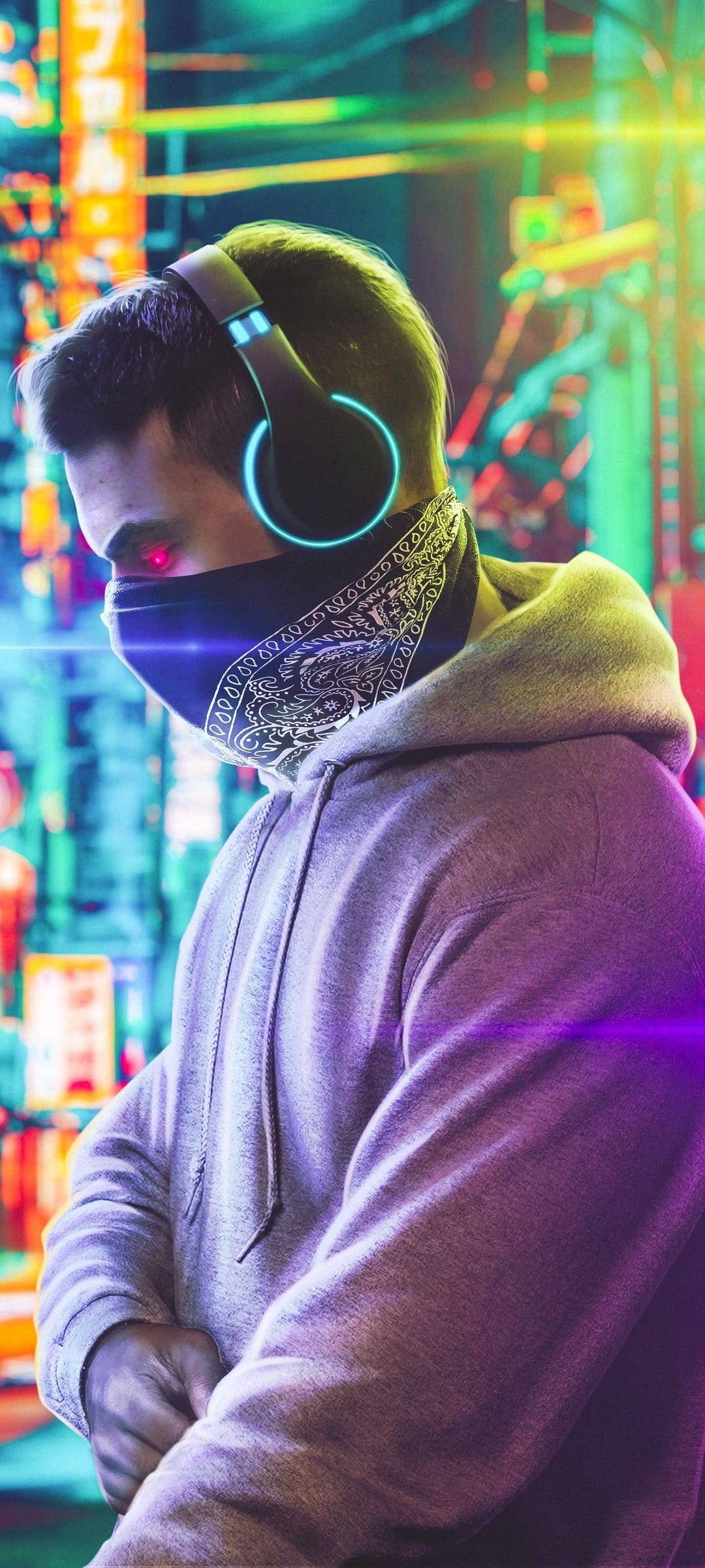 Man in a grey hoodie and paisley bandana with glowing red eyes and blue headphones in a neon-lit urban alleyway.