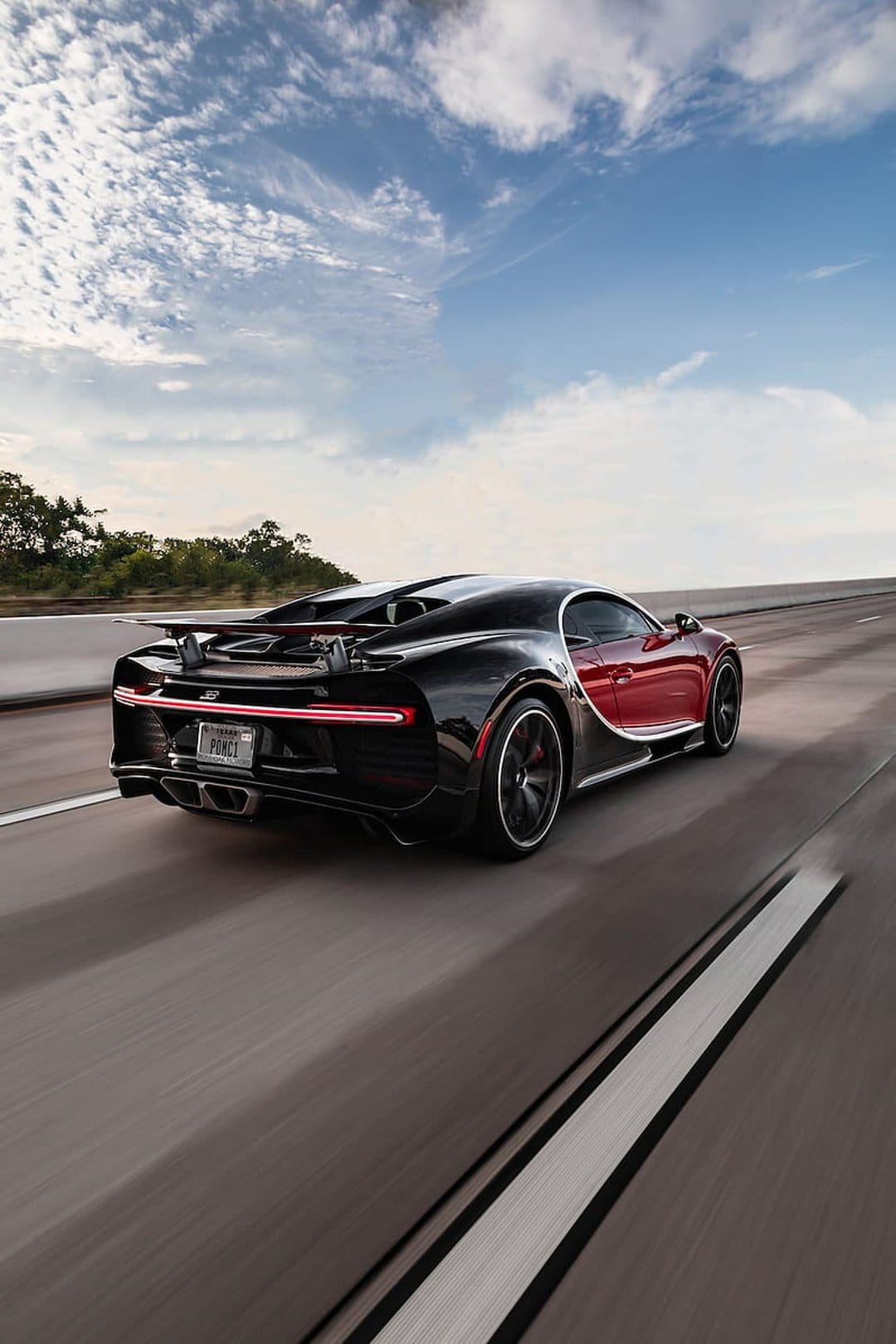 Bugatti Chiron Super Sport with glowing red taillights driving on a highway at dusk under a cloudy sky.