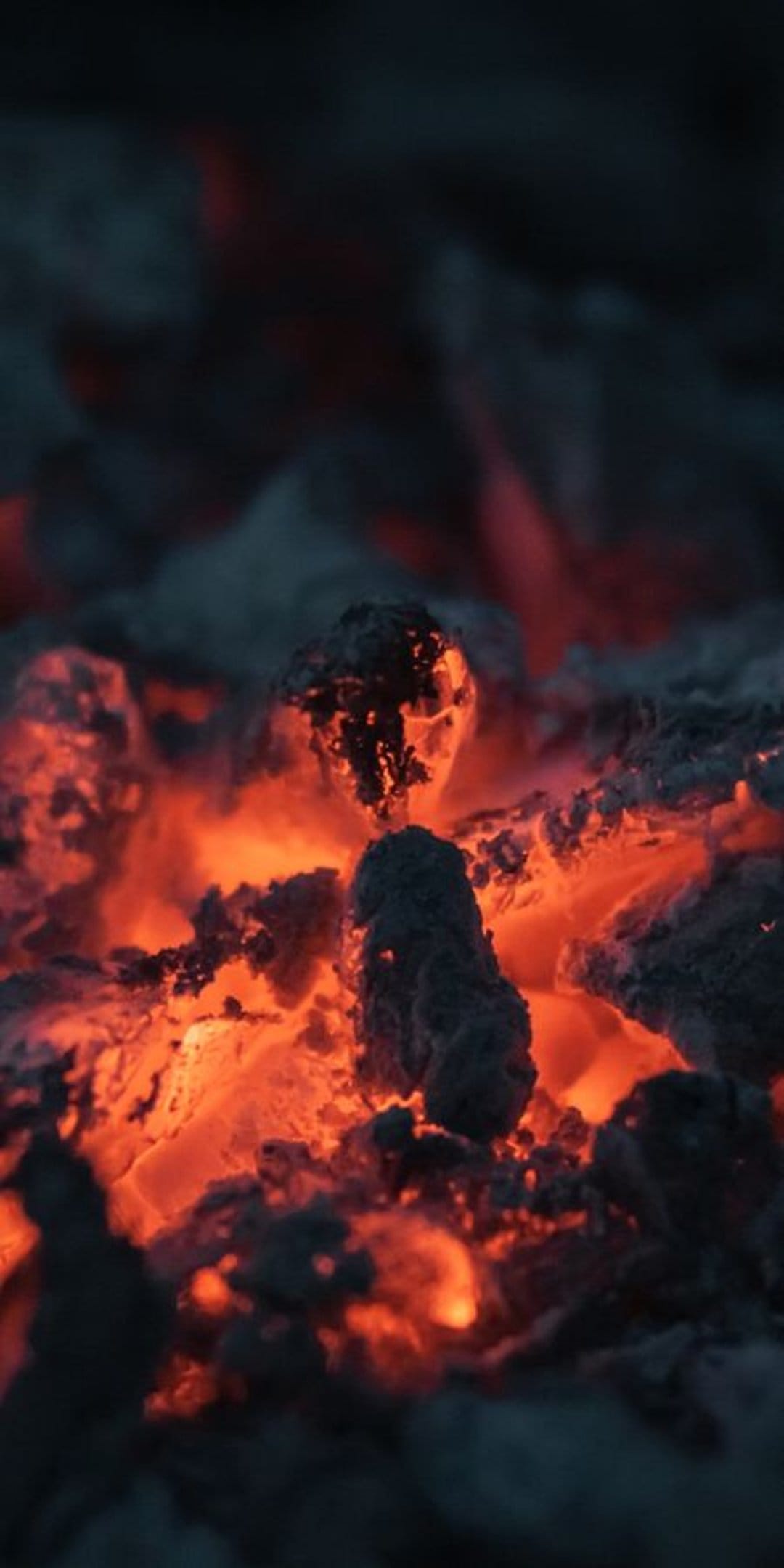 Smoldering red coals and orange embers glow through a layer of dark grey ash with detailed volcanic textures.