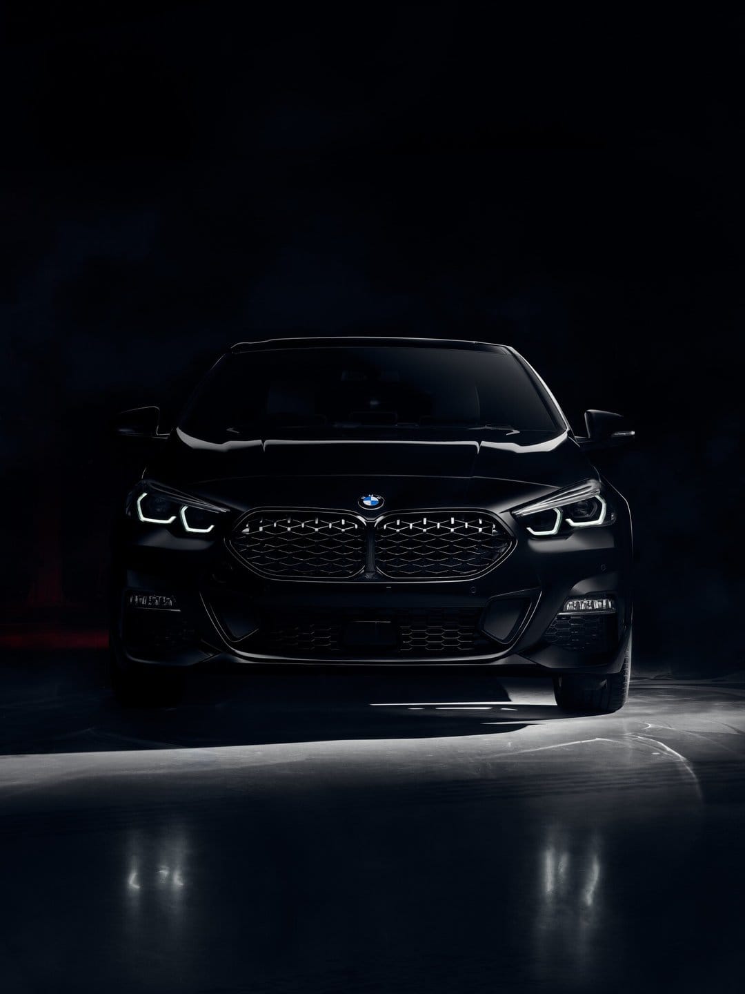 Front view of a black luxury car with glowing white LED headlights against a dark background in a studio.