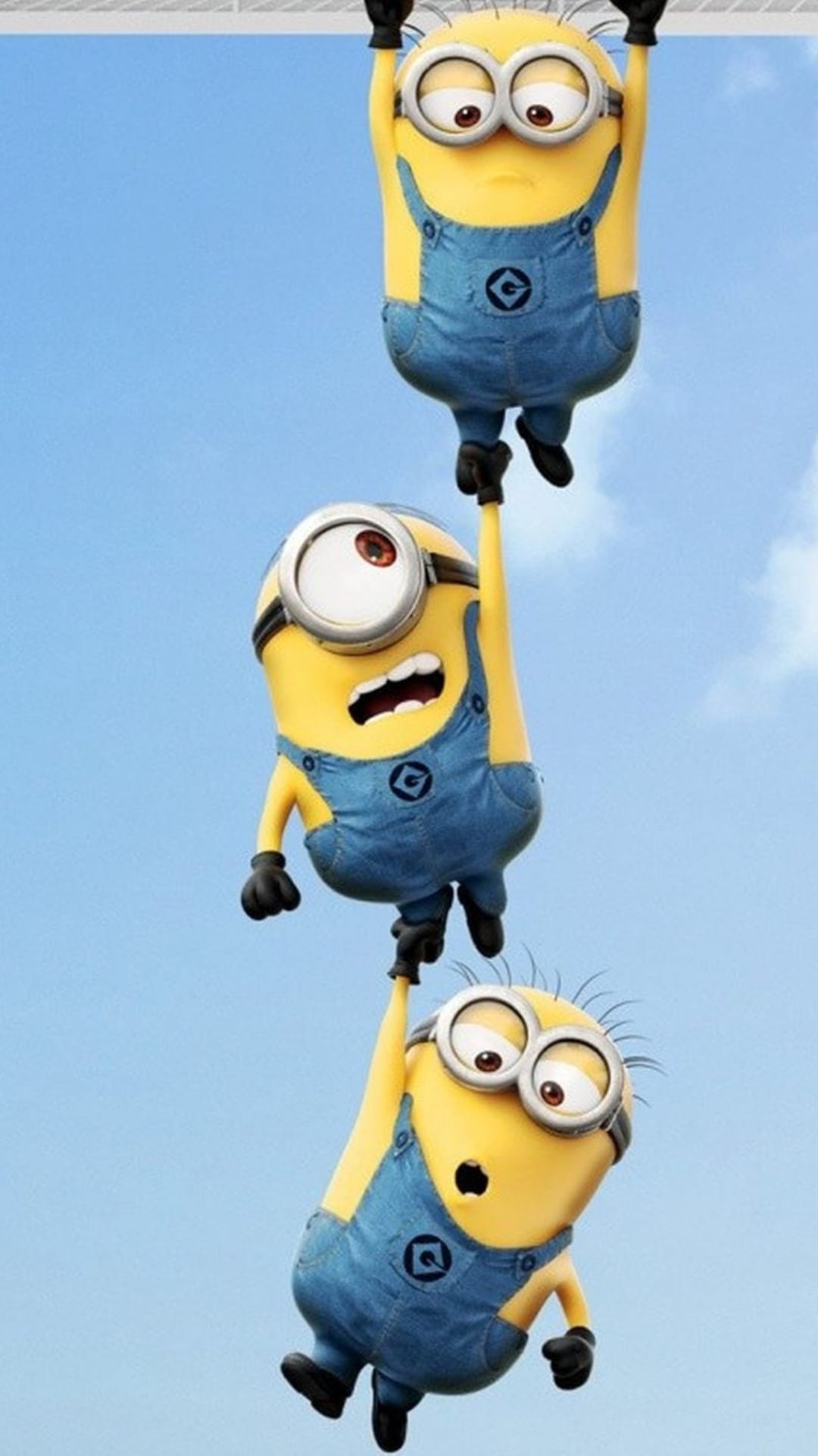 Three yellow Minions in denim overalls hang from a horizontal bar set against a clear and bright blue sky background.