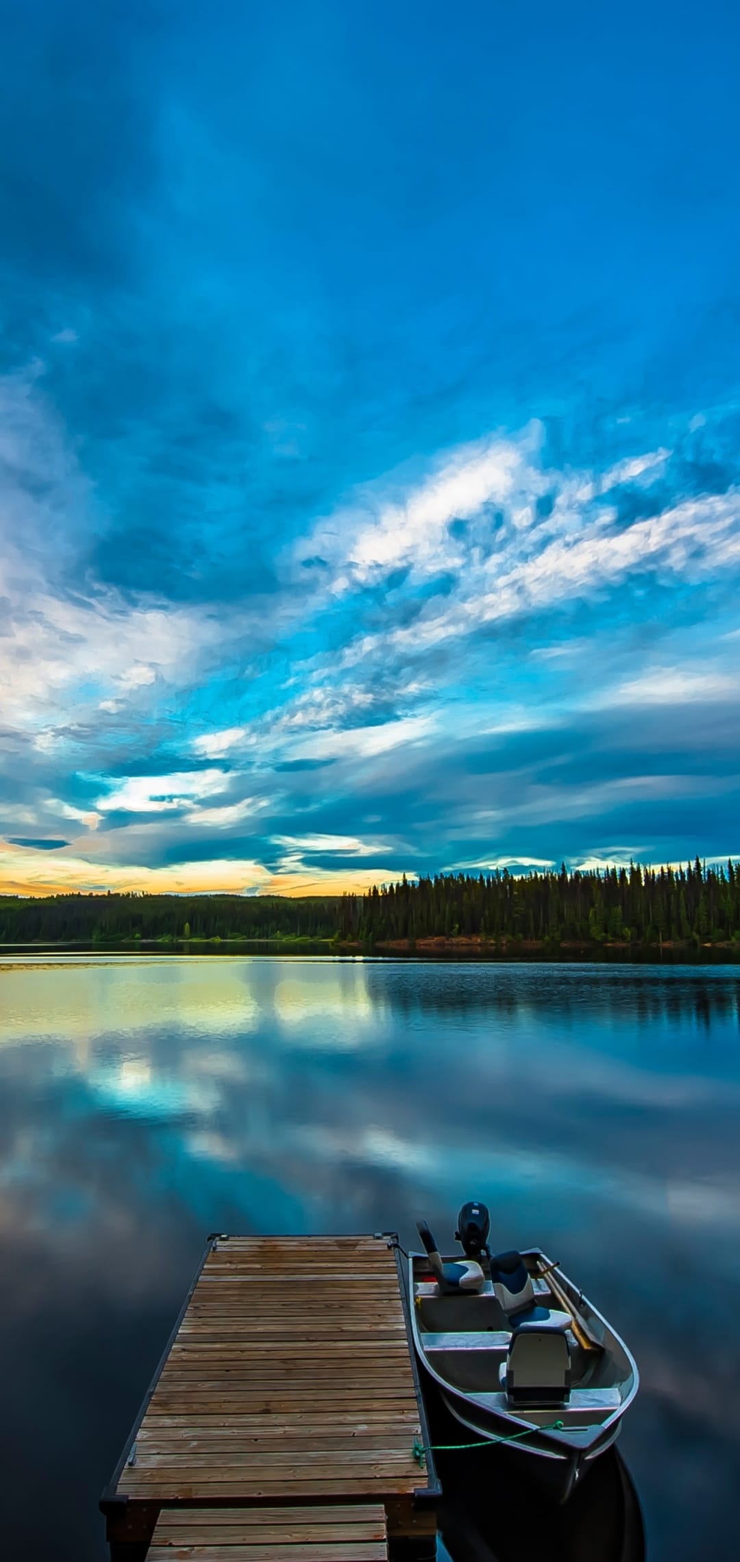 Wooden pier and small boat on a glassy lake with a pink sunset sky and distant forest treeline in the background.