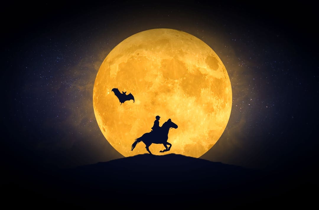 Rider on a galloping horse silhouetted against a colossal orange full moon with bats flying in a starry night sky.