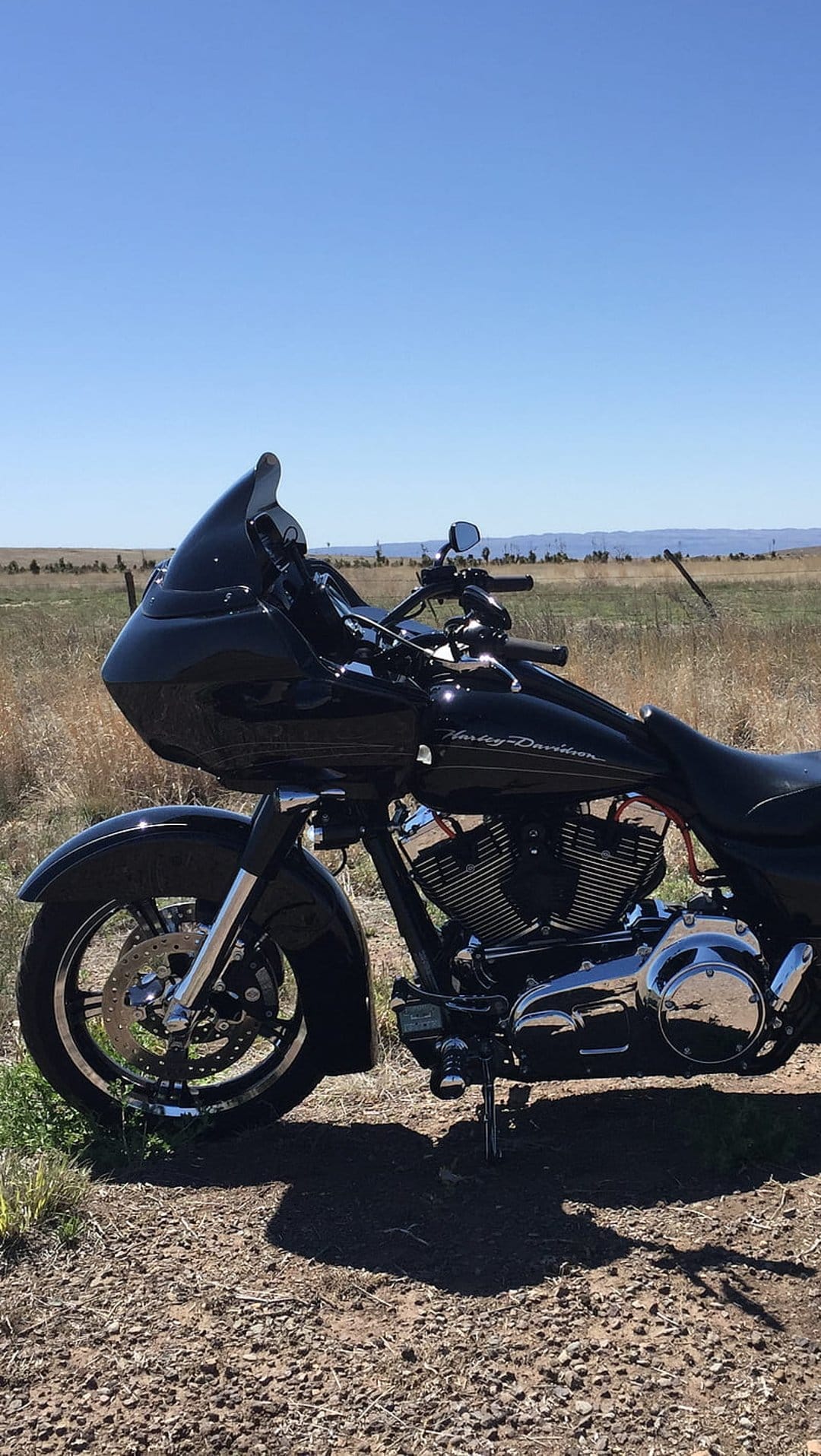 Black Harley-Davidson motorcycle with chrome accents parked on a gravel path under a clear blue summer sky.