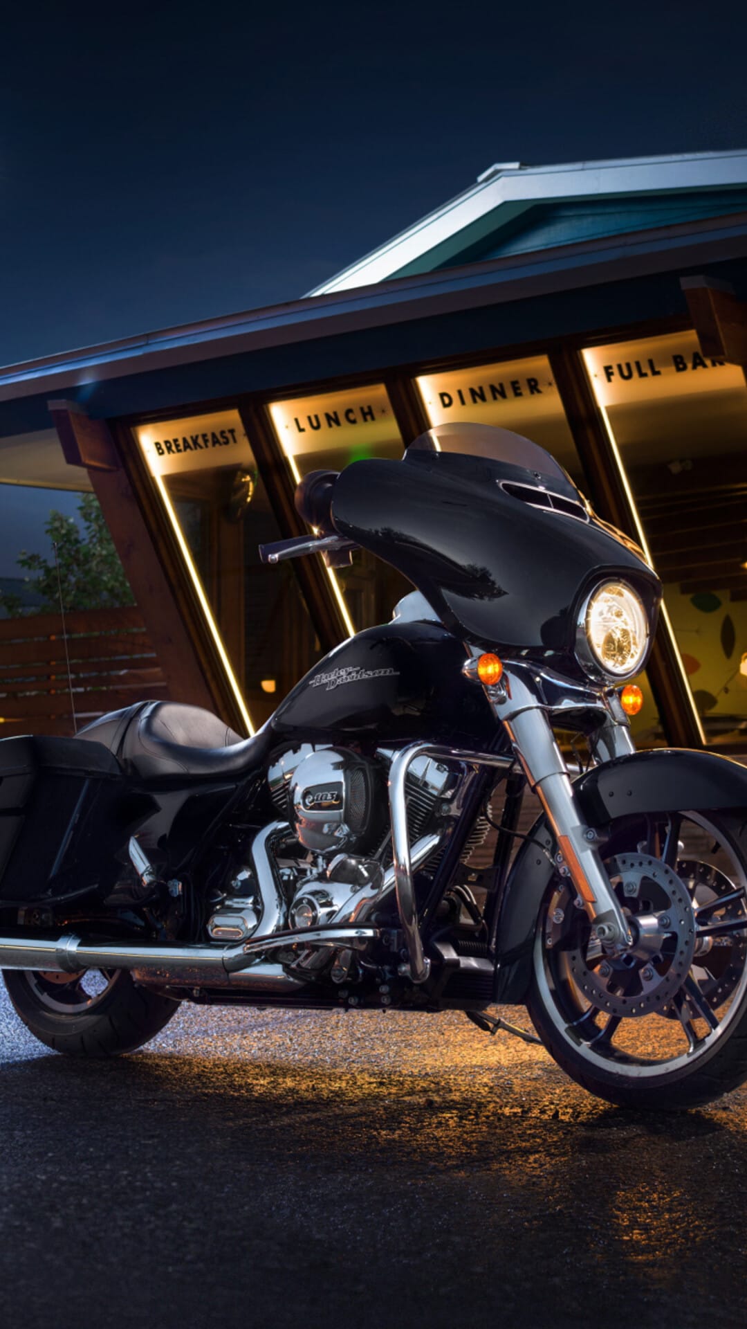 Black cruiser motorcycle with chrome engine parked at a diner with glowing neon signs under a night sky.
