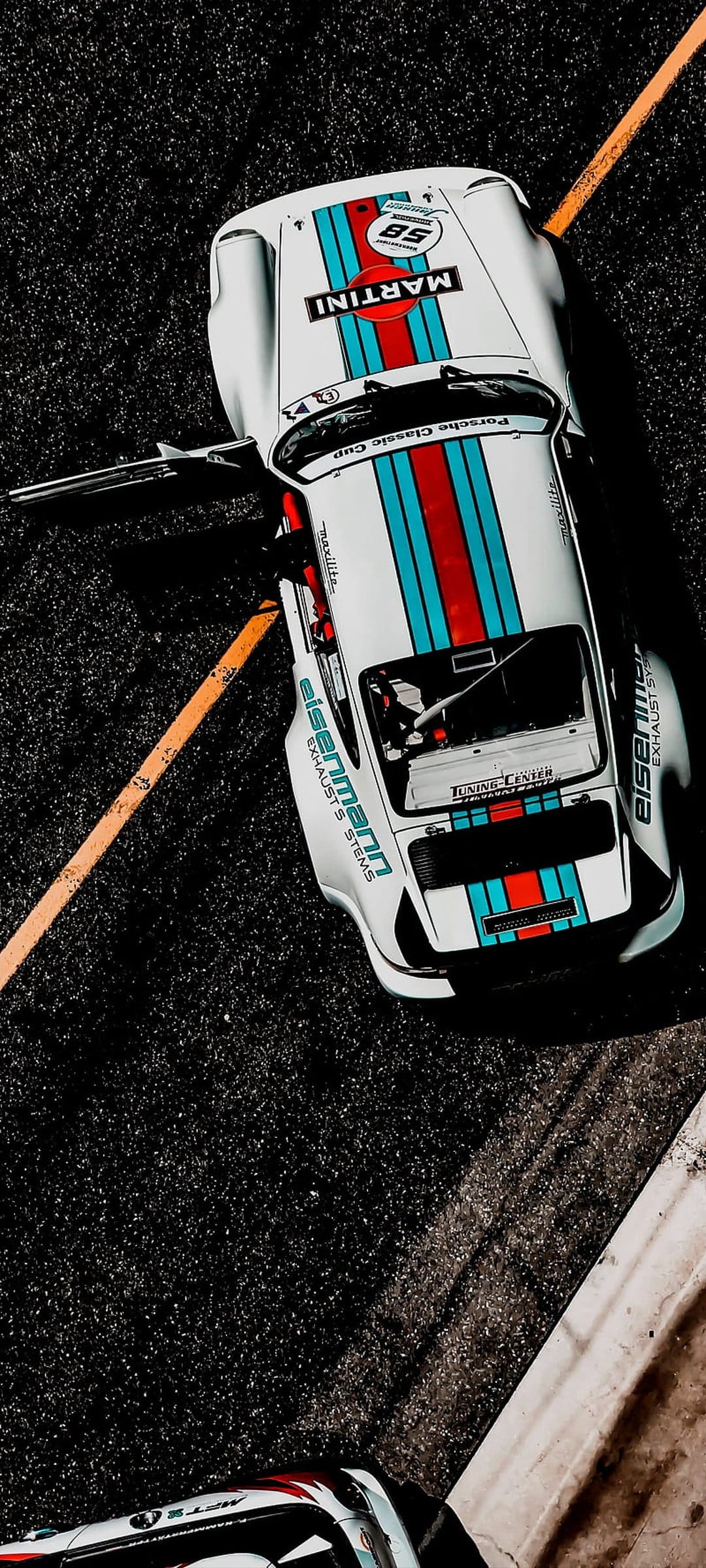White Porsche Classic Cup car with Martini Racing stripes on a dark asphalt track with a bright orange line.