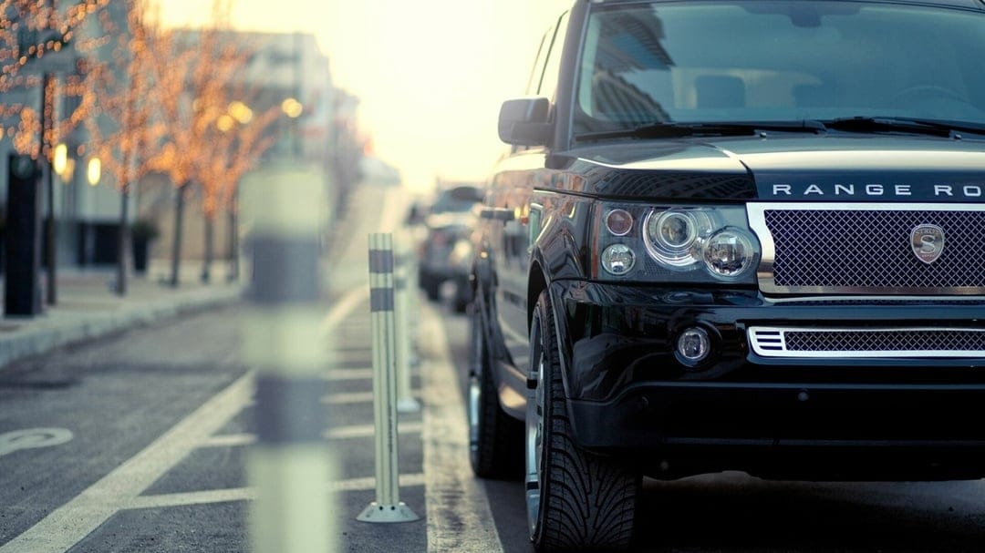 Front view of a black Range Rover with a chrome grille parked on a city street at sunset with warm bokeh.