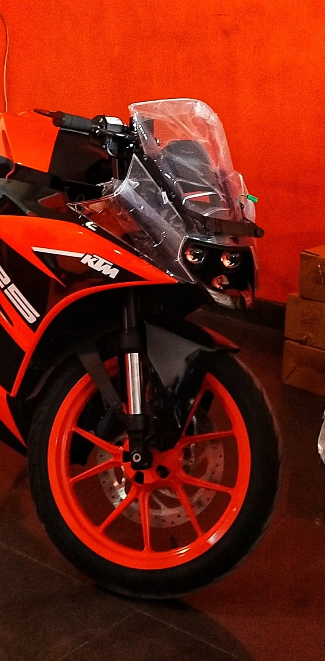 KTM RC 125 motorcycle front fairing with dual headlights, clear windshield, and orange rim against an orange wall.