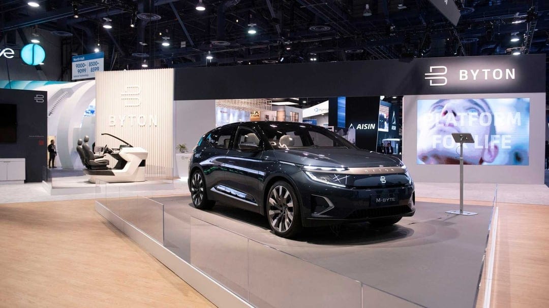 Dark grey Byton M-Byte electric car on a lit platform at a modern automotive technology exhibition booth.