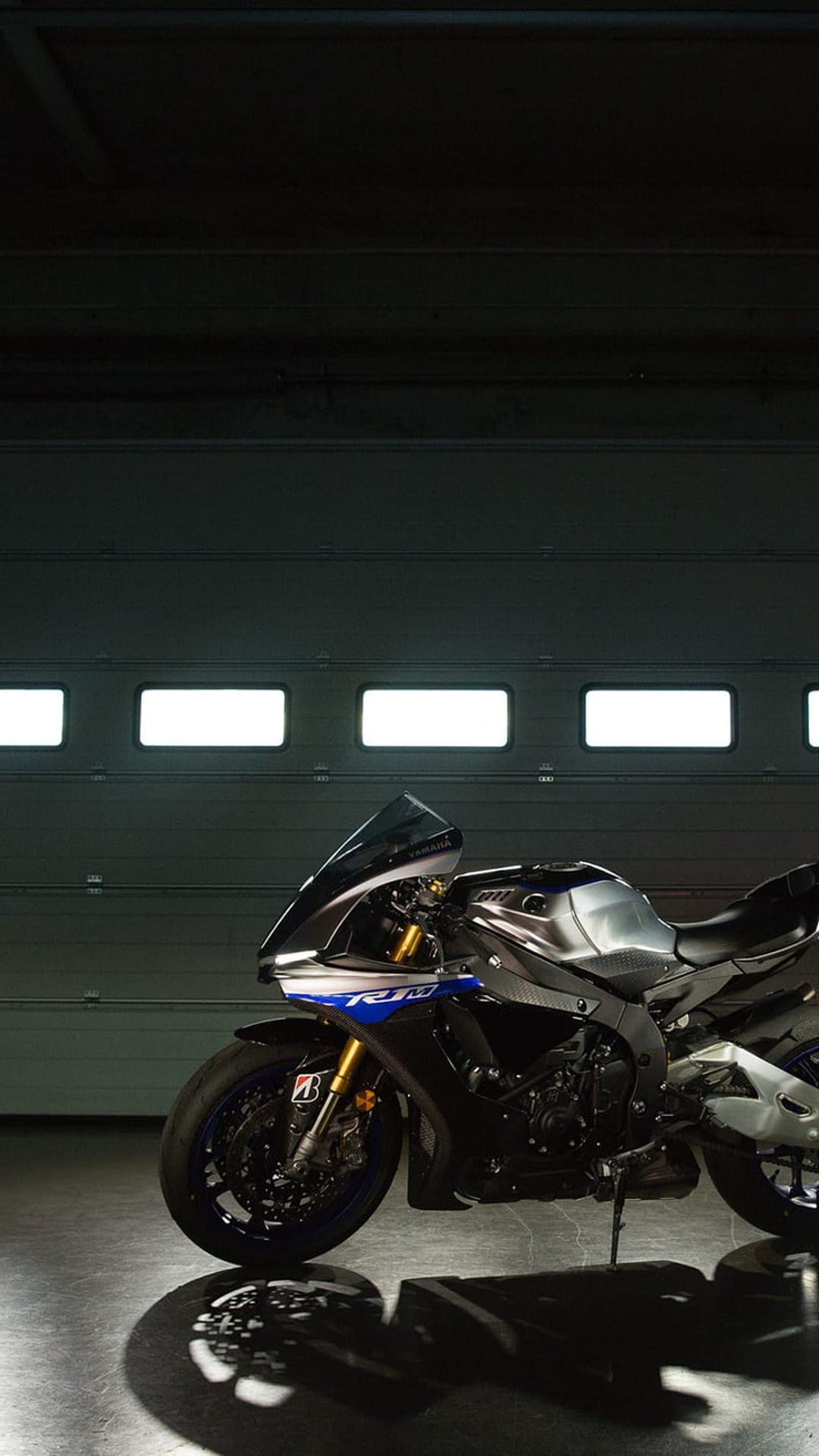 Yamaha R1 sportbike with silver fairings and blue wheels parked inside a dimly lit garage with glowing panels.