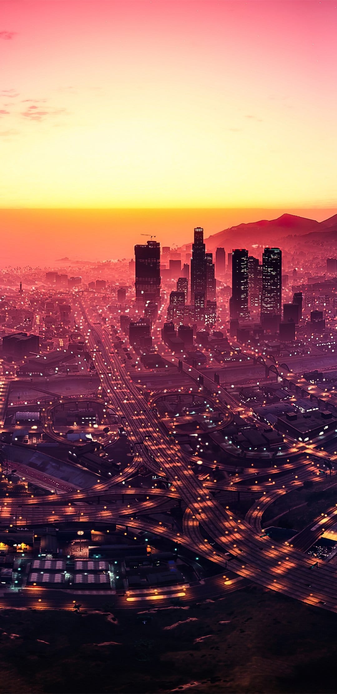 Los Santos city skyline at sunset with illuminated highway interchanges and a pink orange sky aerial view.