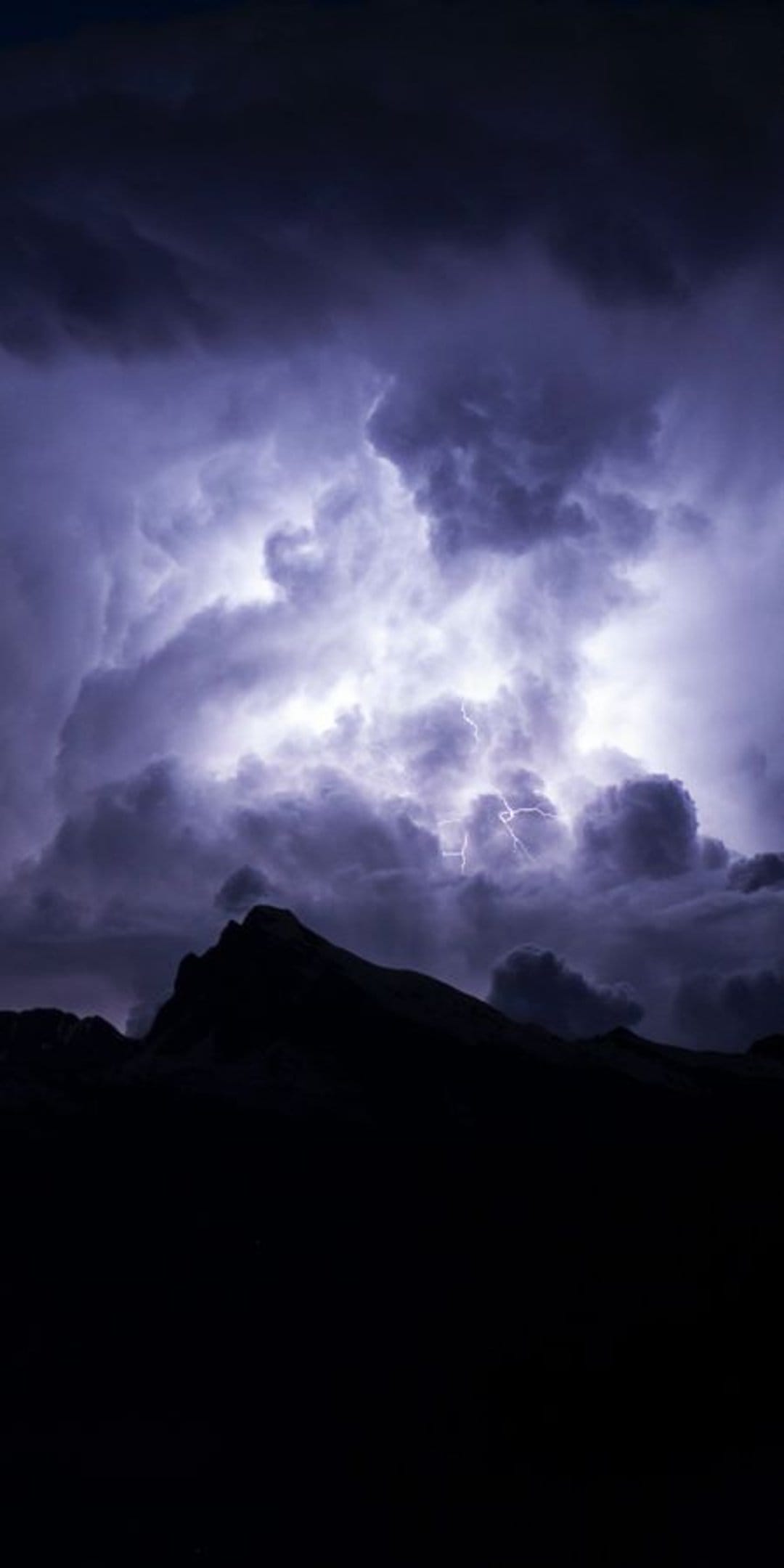 Bright lightning bolt striking through dark storm clouds above the sharp silhouettes of rugged mountain peaks.