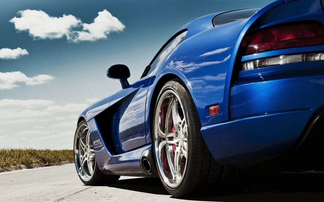 Rear side view of a blue Dodge Viper SRT-10 with chrome rims parked on a road under a bright cloudy sky.