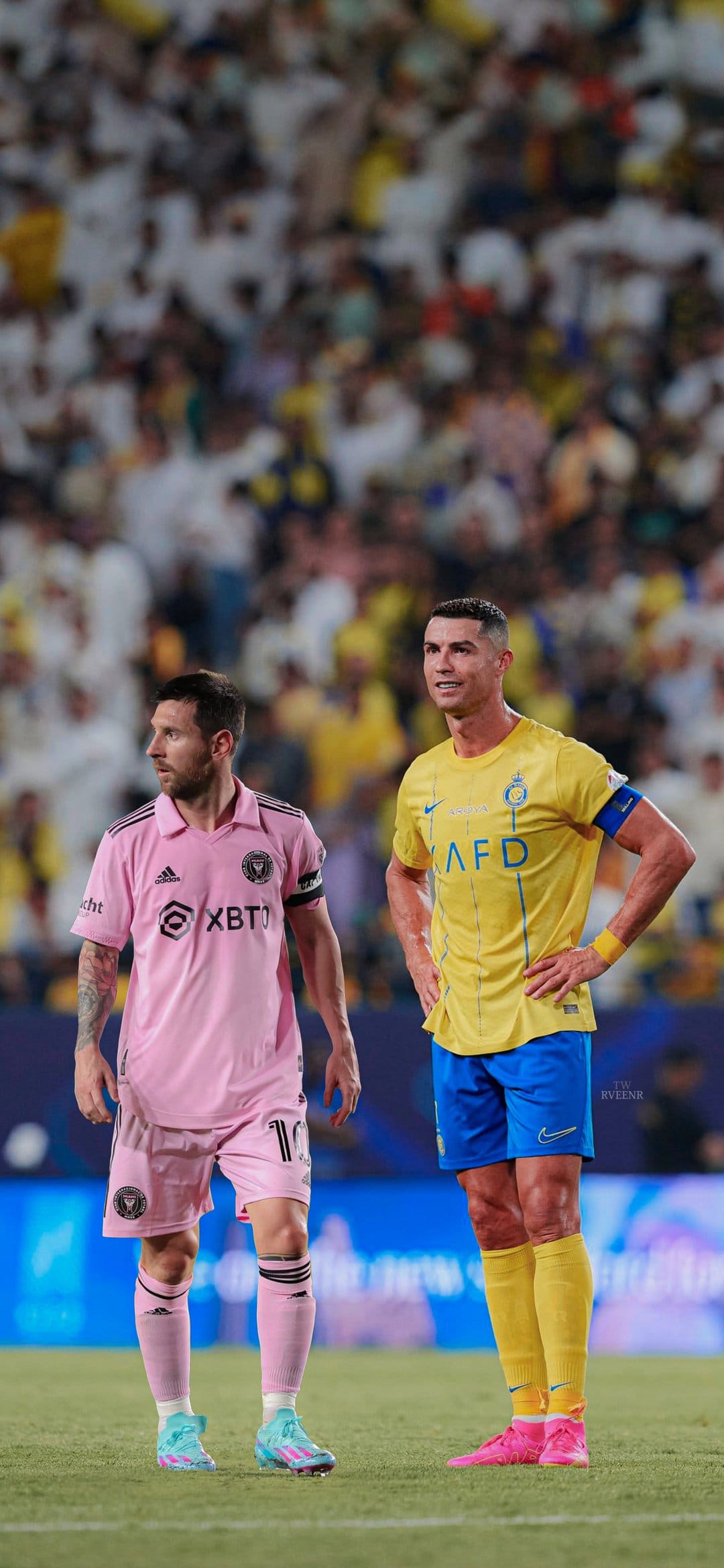 Lionel Messi in pink and Cristiano Ronaldo in yellow stand side by side on a soccer pitch during a match.
